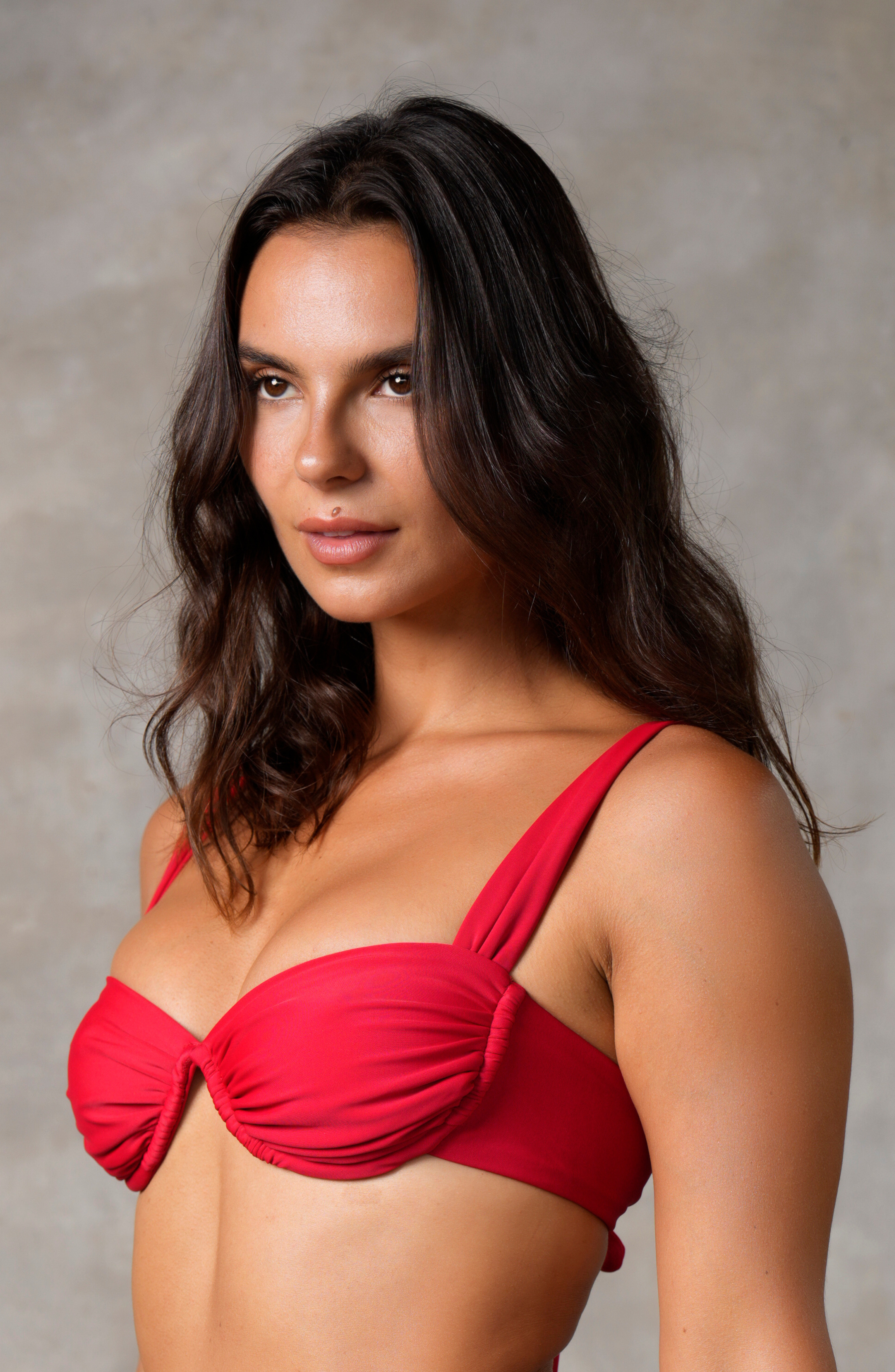 model standing side on against wall wearing red underwire bikini top