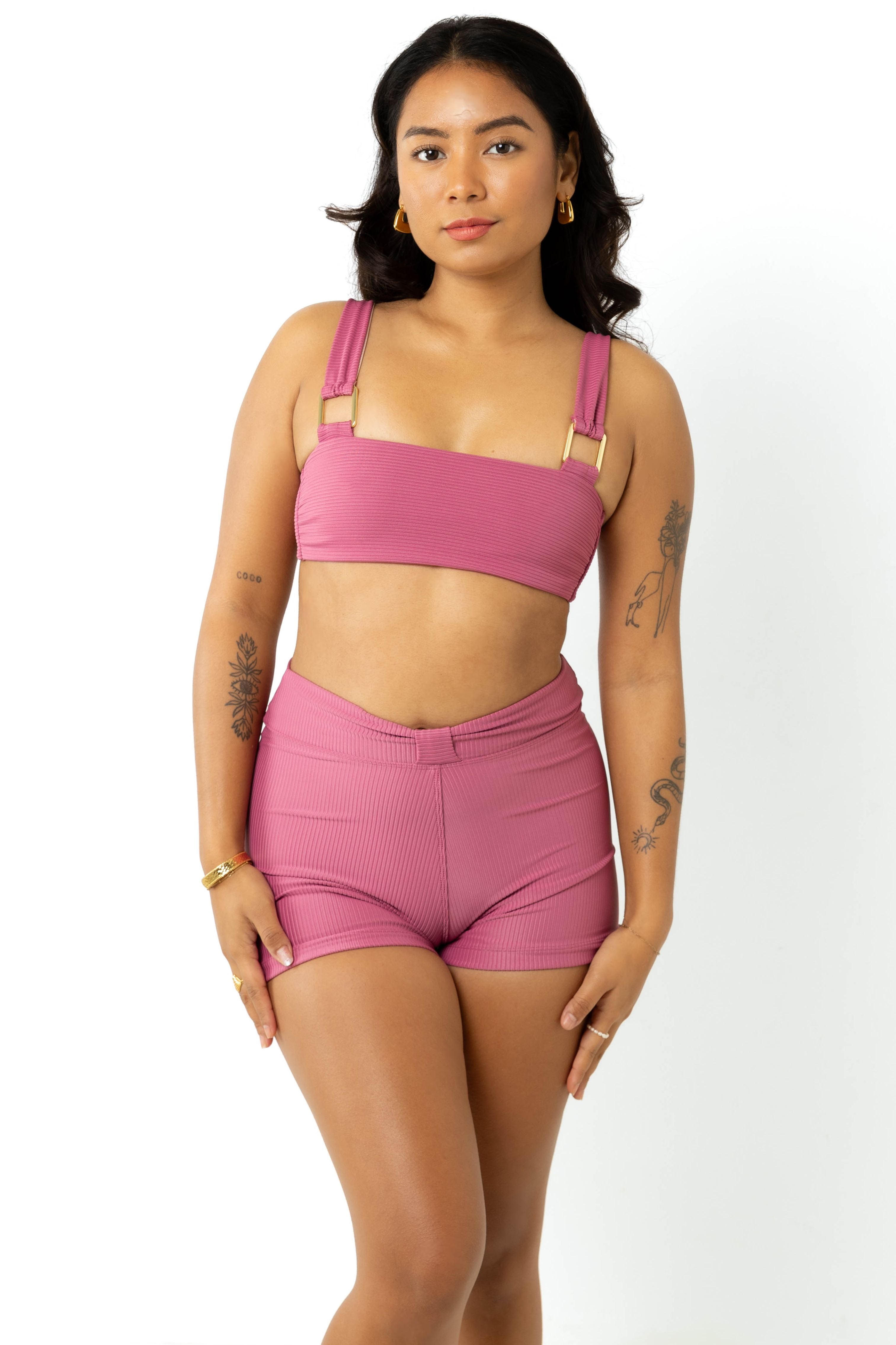 A model wearing a pspice coloured bikini top and high waisted swim shorts, standing in a studio with white background