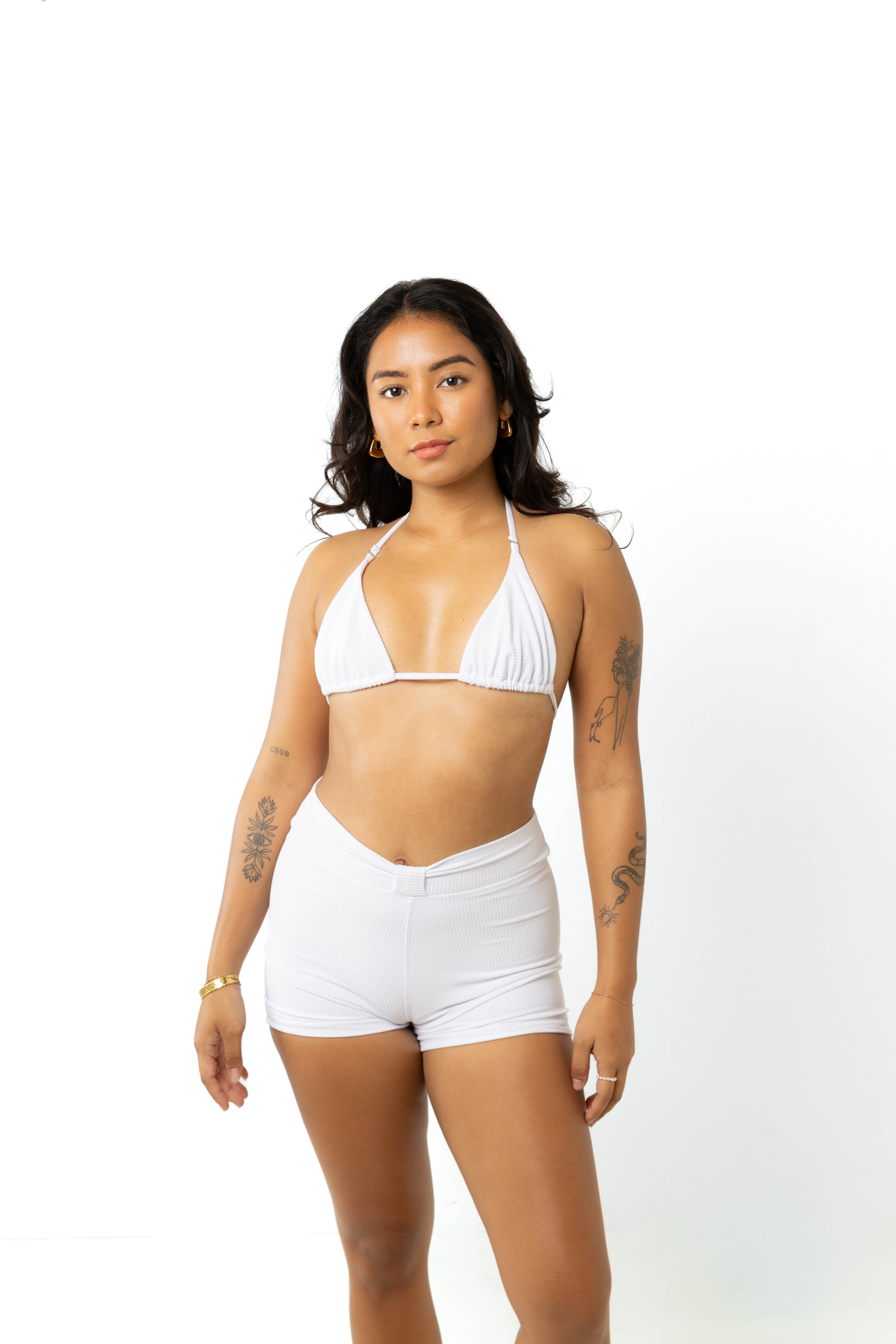 size 6 model standing in studio with white background wearing white triangle bikini top and white high-waisted swim shorts, front view