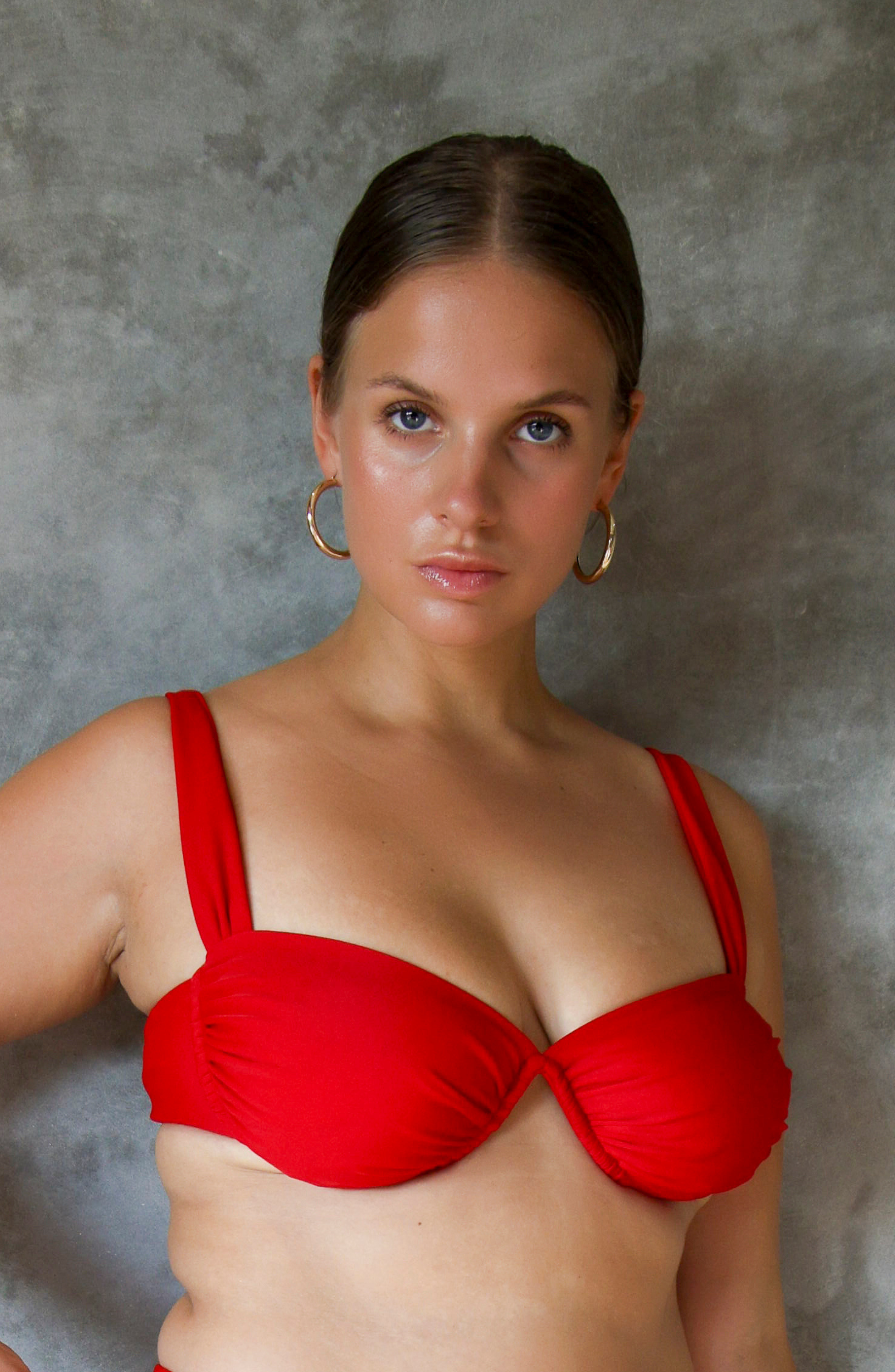 model lizzi standing against wall wearing red underwire bikini top 