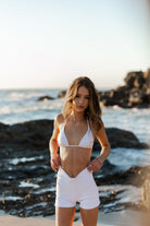 Size 4/6 model wearing the campbell white triangle bikini top and high waisted swim shorts in white at the beach