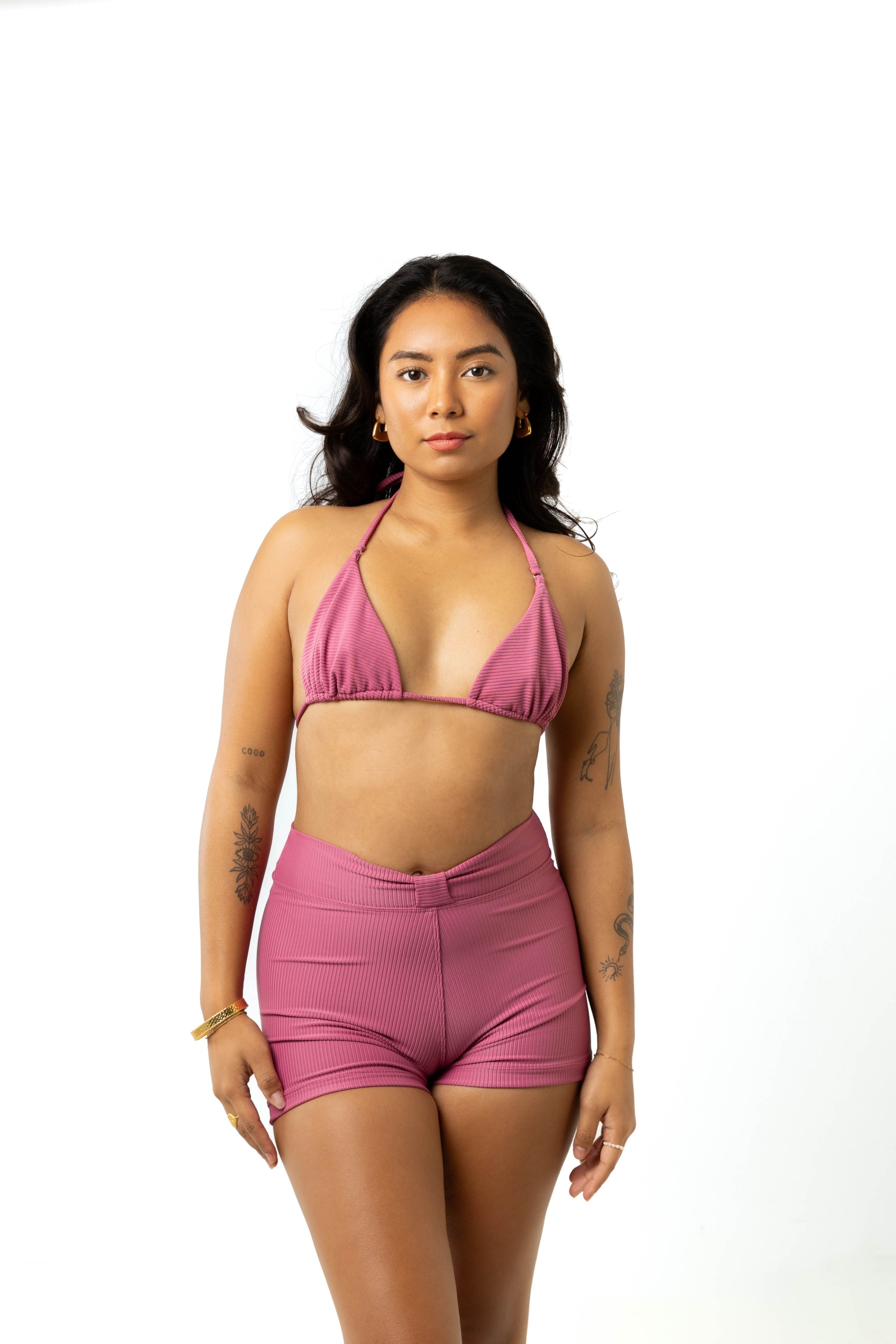 Size 6 model wears spice pink high-waist swim shorts and spice pink triangle bikini while standing against white background