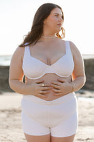 Model posing at beach wearing the white harlow underwire top designed for full bust and campbell swim shorts in white 