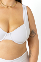 model in a photography studio facing camera, wearing a white ribbed underwire bikini top. This is a close-up image of the material details.