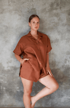 Model poses for photo in Pinksalt Swimwear klum espresso brown Linen shirt and shorts set. This is a front/side view, with her hand in the pocket of the drawstring linen shorts.