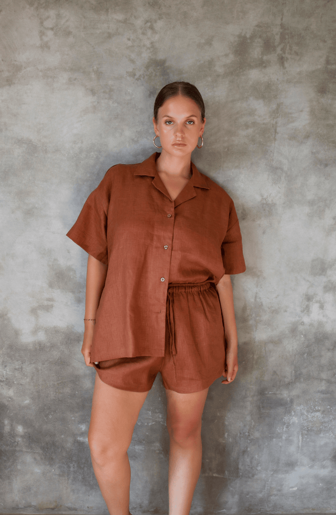 Model poses for photo in Pinksalt Swimwear klum espresso brown Linen shirt and shorts set. This is a front view, with one side tucked in, hands down by her side.