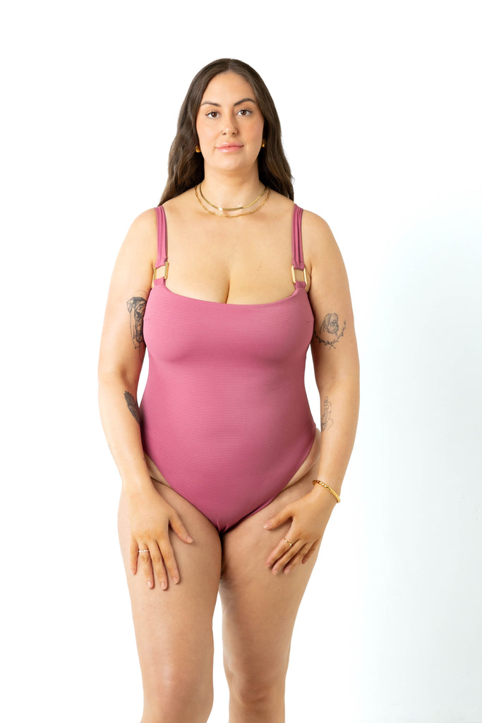 Model size 18 wears spice pink swimsuit with semi thick straps on a white background in a studio. Front view.