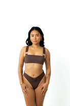 Woman standing in studio with white background wearing chocolate brown yasmeen bikini crop top and high-rise chocolate brown bikini bottoms.