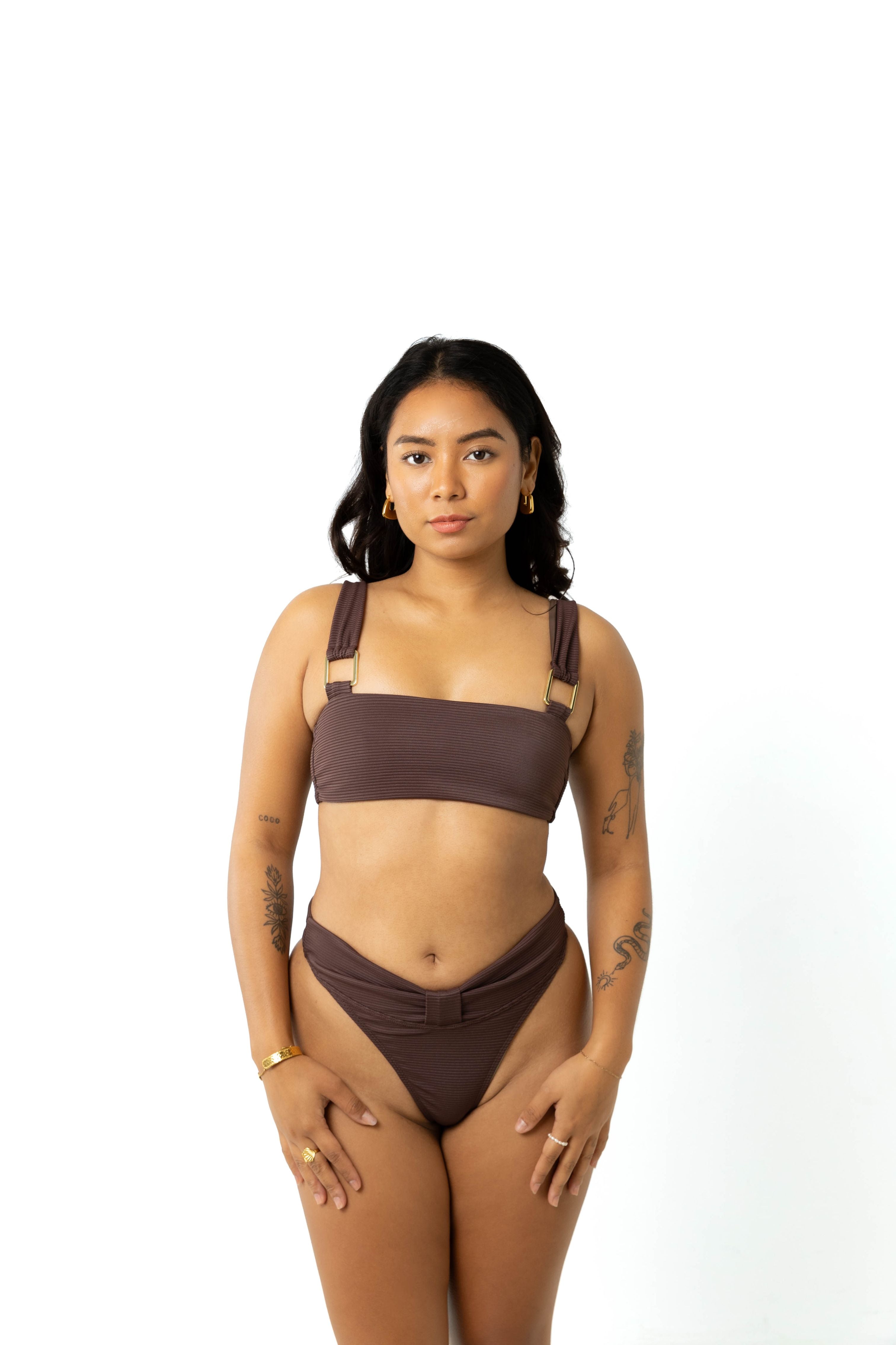 Woman standing in studio with white background wearing chocolate brown yasmeen bikini crop top and high-rise chocolate brown bikini bottoms.