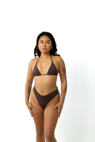 Woman in studio on white background wearing a chocolate brown triangle bikini top and chocolate brown high cut leg bikini bottoms