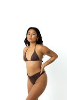 Woman in studio on white background wearing a chocolate brown triangle bikini top and chocolate brown high cut leg bikini bottoms. Side view