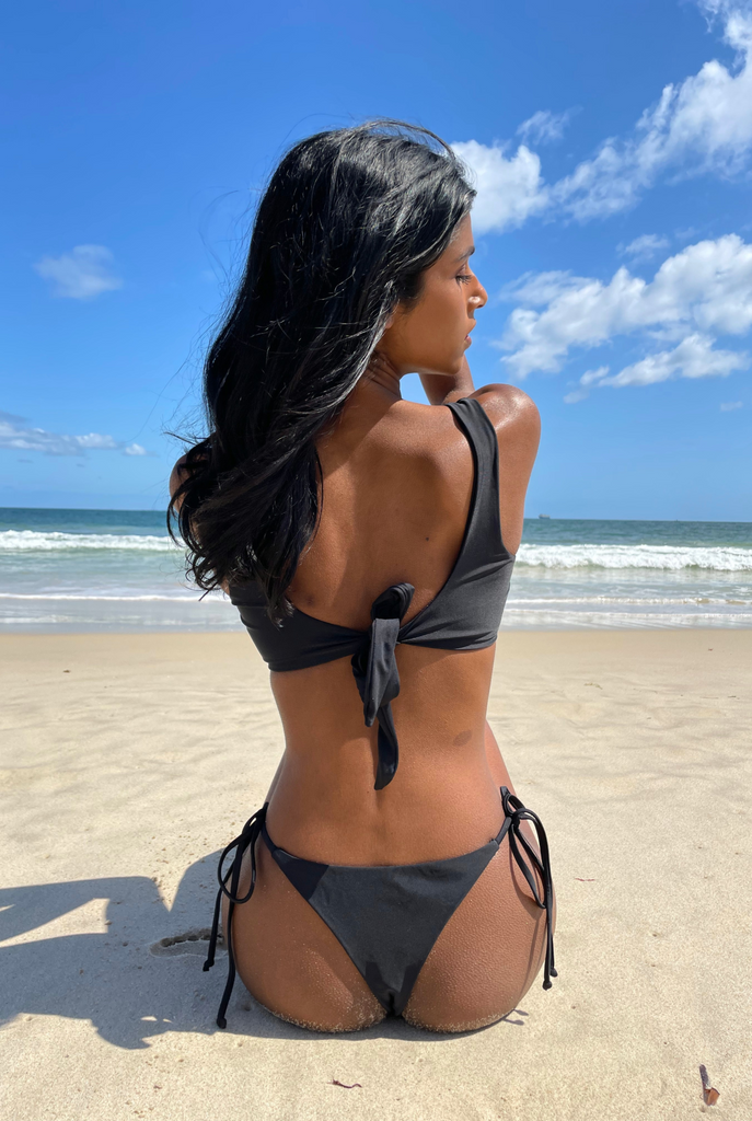 woman sitting on the beach with her back facing the camera wearing a black bikini